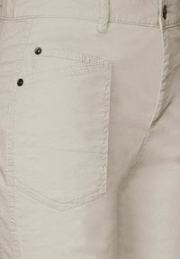 Ljust beige bomullsjeans med en ensam bakficka med svarta knappar och synliga sömdetaljer längs sömmarna.