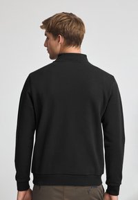 Svart sweatshirt med hög krage, långa ärmar och ribbad nederkant. Tillverkad av mjukt tyg, med en slät textur och minimalistisk design.