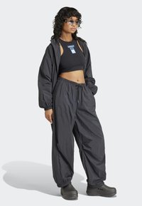 Svart cropped tank topp med logo, kombinert med løse svarte joggebukser og svarte klogs. Materialet ser lett og teksturert ut.