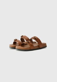 Brune sandaler laget av syntetisk materiale. To brede stropper med spenner, en flat såle og et enkelt design. Glatt tekstur.