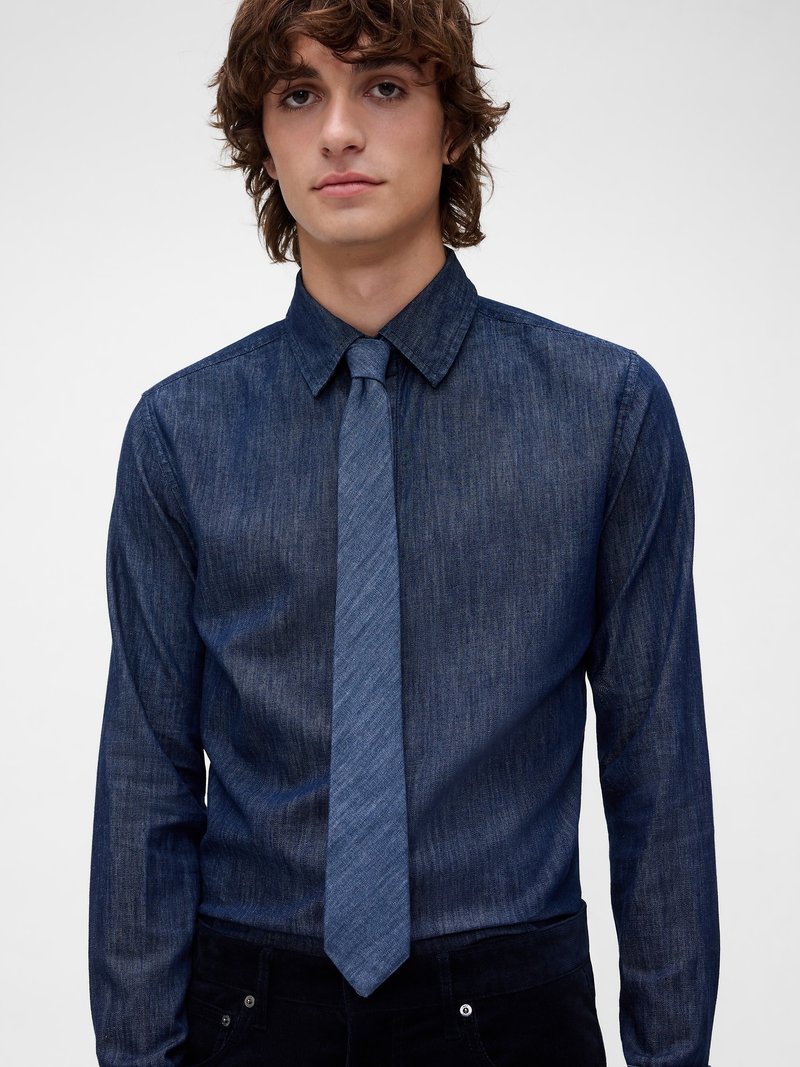 Chemise en denim bleu foncé avec un col structuré et des manches longues, associée à une cravate slim assortie en tissu denim plus clair.