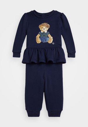 Στρατιωτικού μπλε σύνολο δύο τεμαχίων με μπλούζα που έχει περφορέ και σχέδιο από αρκουδάκι, σε συνδυασμό με αντίστοιχες φόρμες και ριγέ μανσέτες.