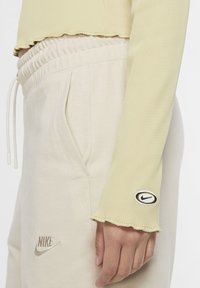 Ljusgrön ribbad långärmad topp med en fransad nederkant, parat med beigefärgade sweatpants som har sidofickor och en broderad Nike-logotyp.