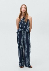 Joncs en marine et blanc avec un décolleté halter, des jambes larges et des motifs géométriques. Le tissu semble lisse avec une texture légère.
