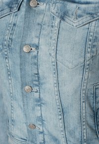 Lichtblauwe spijkerjasje met metalen knopen en een gestikte borstzak aan de linkerkant.