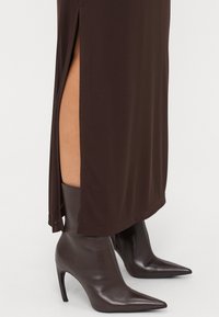 Brun midi-kjole med side-splitter, parret med brune lærstøvler med spiss tå, med en glatt tekstur og en strømlinjeformet silhuett.