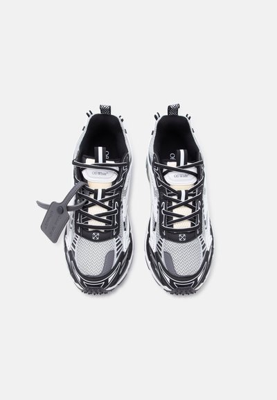 Ζευγάρι αθλητικών παπουτσιών σε μαύρο, γκρι και λευκό χρώμα με ύφασμα από δίχτυ, με το εμπορικό σήμα "Off-White", που διαθέτουν μαύρα κορδόνια και γκρι ετικέτα στο αριστερό παπούτσι.