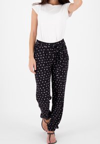 Svartmönstrade byxor med rosa fågmotiv, lätt material, elastisk midja, sida fickor och en avslappnad passform, kombinerat med en vit t-shirt.