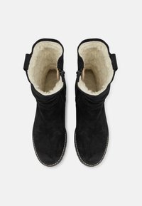 Bottines en suède noir avec doublure beige douce, texture froncée sur le dessus et couture contrastante le long de la semelle. Fermeture à glissière sur le côté.