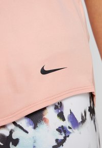 Jasnoróżowy sportowy top z czarnym logo Nike, w połączeniu z legginsami w abstrakcyjne wzory z motywami kwiatowymi.