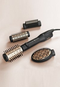 Strumento per acconciare i capelli neri con dettagli dorati e cilindri texturizzati. Include tre spazzole rimovibili, caratterizzate da diversi modelli di setole.