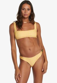 Set bikini giallo e rosa a quadri composto da un top con scollo quadrato e uno slip a vita bassa, realizzato in tessuto liscio e elastico.