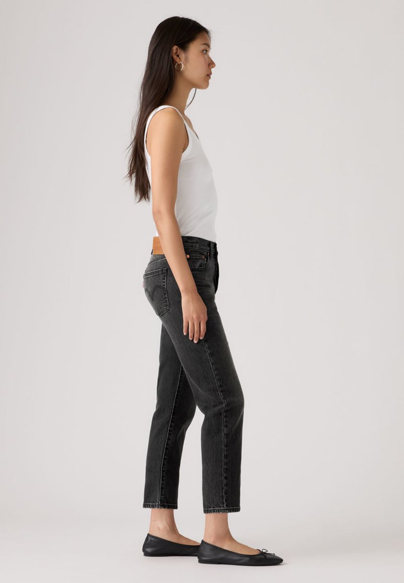 Black denim jeans with a straight cut, high waist, and slight faded texture, paired with a white tank top and black ballet flats.