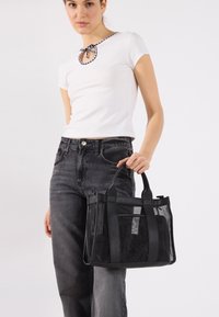 Saco tote preto com uma mistura de rede transparente e tecido sólido. Apresenta alças robustas e uma forma elegante e estruturada. Adequado para uso diário.