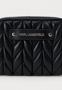 Μαύρο δερμάτινο πορτοφόλι με ραφή και μεταλλική πλάκα που φέρει την ένδειξη "KARL LAGERFELD", συνδεδεμένη με δύο ασημένιες βίδες.