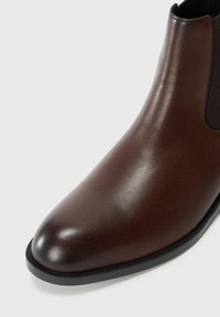 Brown leather chelsea boot with a smooth finish, elastic side panels, and a black rubber sole. Pointed toe design.