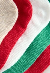 Vier übereinander gestapelte Strickstoffstücke in den Farben Rot, Weiß, Grün und Creme mit einer strukturierten, weichen Oberfläche. Jedes Stück hat eine glatte Kante.