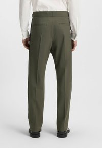 Olivgrüne Hosen mit maßgeschneidertem Schnitt, ausgestattet mit zwei Gesäßtaschen und seitlichen Streifen, die entlang der Beine verlaufen. Glatte Textur und keine sichtbaren Muster.