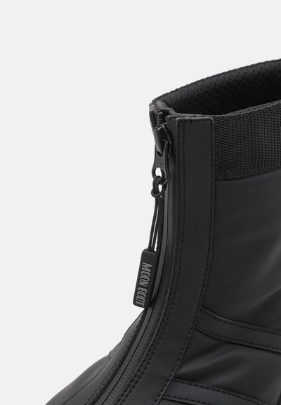 Botte étanche noire avec une finition lisse, fermeture éclair, poignet élastique texturé et étiquette de marque. Conception à plusieurs panneaux pour la structure.