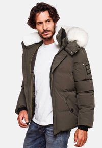 Green padded jacket with a fur-lined hood, zip closure, side pockets, and ribbed cuffs. Features a patch on the left sleeve.