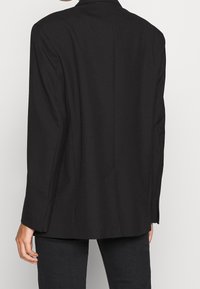 Svart kavaj med långa ärmar, strukturerade axlar och rak passform. Slät tyg, enkelt bakventil och ingen synlig hårdvara.