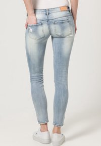 Light blue skinny jeans featuring a faded wash, distressed detailing on the back pocket, and a branded leather patch at the waistband.