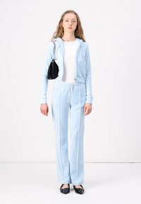 Lichtblauwe velours trainingsbroek met een hoodie-jack en een broek met een trekkoord, gecombineerd met een kleine zwarte handtas en zwarte flats met versieringen.