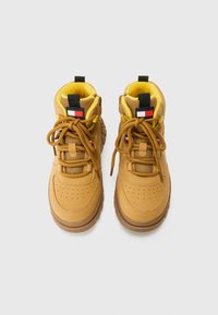 Zapatillas de baloncesto altas de cuero marrón con detalles de malla, forro de felpa amarilla, puntera perforada y parche de logo negro en la lengua.