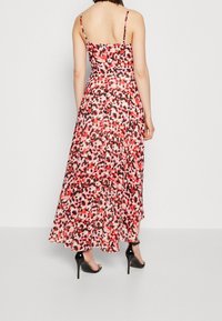 Maxiklänning med justerbara tunna band, med ett flerfärgat abstrakt mönster i nyanser av röd och svart, tillverkad av lätt tyg.