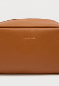 Καφέ ορθογώνια θήκη από συνθετικό δέρμα με ανάγλυφο λογότυπο "JACK & JONES", λεία υφή και επάνω φερμουάρ κλεισίματος.