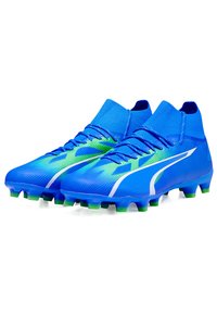 Scarpe da calcio blu con un design testurizzato, caratterizzate da accenti verdi e un colletto alla caviglia in maglia. La suola ha diversi tacchetti per la presa.