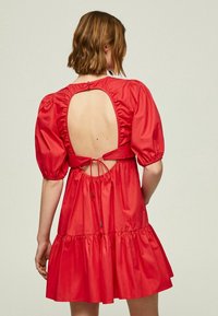 Vestido rojo con mangas abullonadas, espalda al aire y detalle de lazo. Cuenta con una falda de volantes y tela suave y brillante.