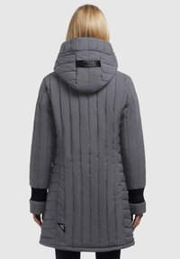 Kvinde set fra ryggen iført en grå quilted hættejakke med lodrette syninger og sorte ribbede manchetter.