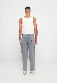 Lichte grijze denim cargo pants met grote zijzakken, een gestructureerde afwerking en een patch op de achterkant. Draagt met een wit tanktop.