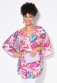 Blusa colorata con motivo floreale, scollatura a V e maniche fluide, abbinata a una pochette trapuntata viola chiaro.