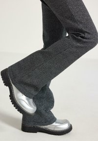 Grå teksturerede flared bukser kombineret med skinnende sølvfarvede sko med en robust sort sål. Outfitet præsenterer et moderne kontrast af materialer.