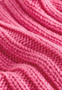 Fluffy roze gebreide stof met een gestructureerd patroon, waarbij dikke en dunne garens in verhoogde steken zijn verweven, wat een golvend uiterlijk creëert.
