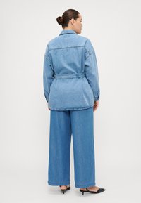 Denim jacket with belt, light blue color, relaxed fit, long sleeves, and back yoke detail, paired with wide-leg light blue denim pants.