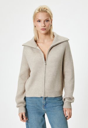 Beige ribbed knit cardigan with a large collar, zippered front, and long sleeves. Made from soft material, featuring a slightly relaxed fit.