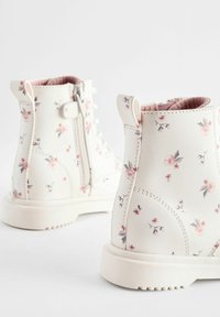 Hvide ankelstøvler lavet af syntetisk læder, dekoreret med et blomstermønster i pink og grøn. Har en sidelukning med lynlås og en struktureret sål.
