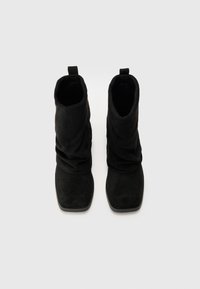 Botas de tornozelo em camurça preta com um design descaído, ponta quadrada, e uma aba na parte de trás. Superfície texturizada e acabamento suave.