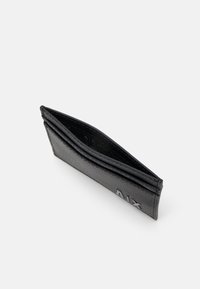 Schwarze Lederbörse mit strukturierter Oberfläche, schlankem Design und geprägtem Branding auf der Vorderseite. Geöffnet, um die Kartenfächer im Inneren zu zeigen.