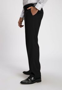 Zwarte pantalon met een getailleerde pasvorm, zijzakken en een gladde stof. Gecombineerd met zwarte nette schoenen, die een slank ontwerp tonen.