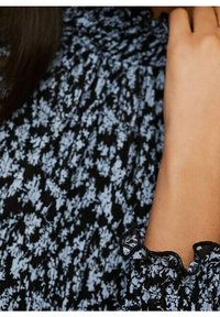 Tissu noir avec un petit motif floral bleu clair, doté de poignets à volants et de détails à froufrous, créant un aspect texturé.