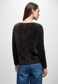 Pullover scuro e morbido con scollo ampio e maniche lunghe, abbinato a jeans in denim blu, visto da dietro su uno sfondo chiaro.