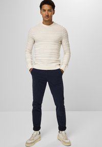 Krämfärgad ribbad långärmad tröja, marinblå chinos och beige sneakers med ljusa accenter. Minimalistisk design; avslappnad passform med vikta ärmslut.
