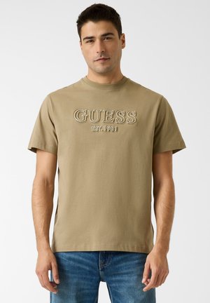Khaki bawełniany t-shirt z okrągłym dekoltem i krótkimi rękawami. Na przodzie wyhaftowany napis "GUESS EST.1981".