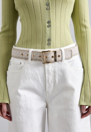 Cintura di crema con hardware dorato e banda decorata, indossata sopra jeans bianchi e una maglietta a coste verde chiaro con bottoni e maniche lunghe.