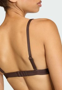 Brązowy stanik z materiału z regulowanymi, prążkowanymi ramiączkami. Posiada płaski zamek oraz gładką teksturę, eksponując projekt pleców.