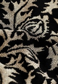 Tessuto nero con un intricato motivo floreale dorato, caratterizzato da una trama testurizzata che conferisce profondità e interesse visivo.